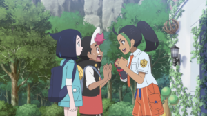 Nemona poses energetically in front of Roy, who looks taken aback, and Liko, the two protagonists of the Pokémon Horizons anime. Nemona wears her orange-and-white school uniform, just like in Pokémon Scarlet.