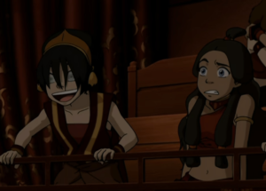 Toph looking absolutely jazzed, while Katara eyes her quizzically, in theater seats in Nickelodeon’s Avatar: The Last Airbender.