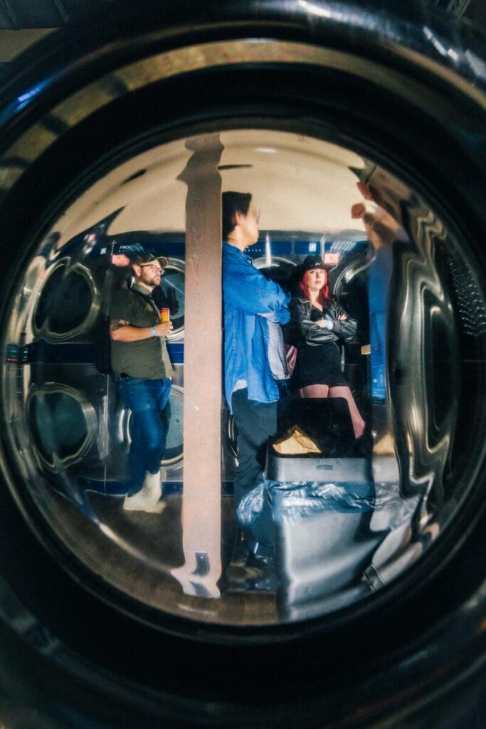 Attendees at Laundry Wand seen through one of the round, portal-like doors to a laundry machine.
