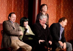 Five people sitting on a stage laughing.