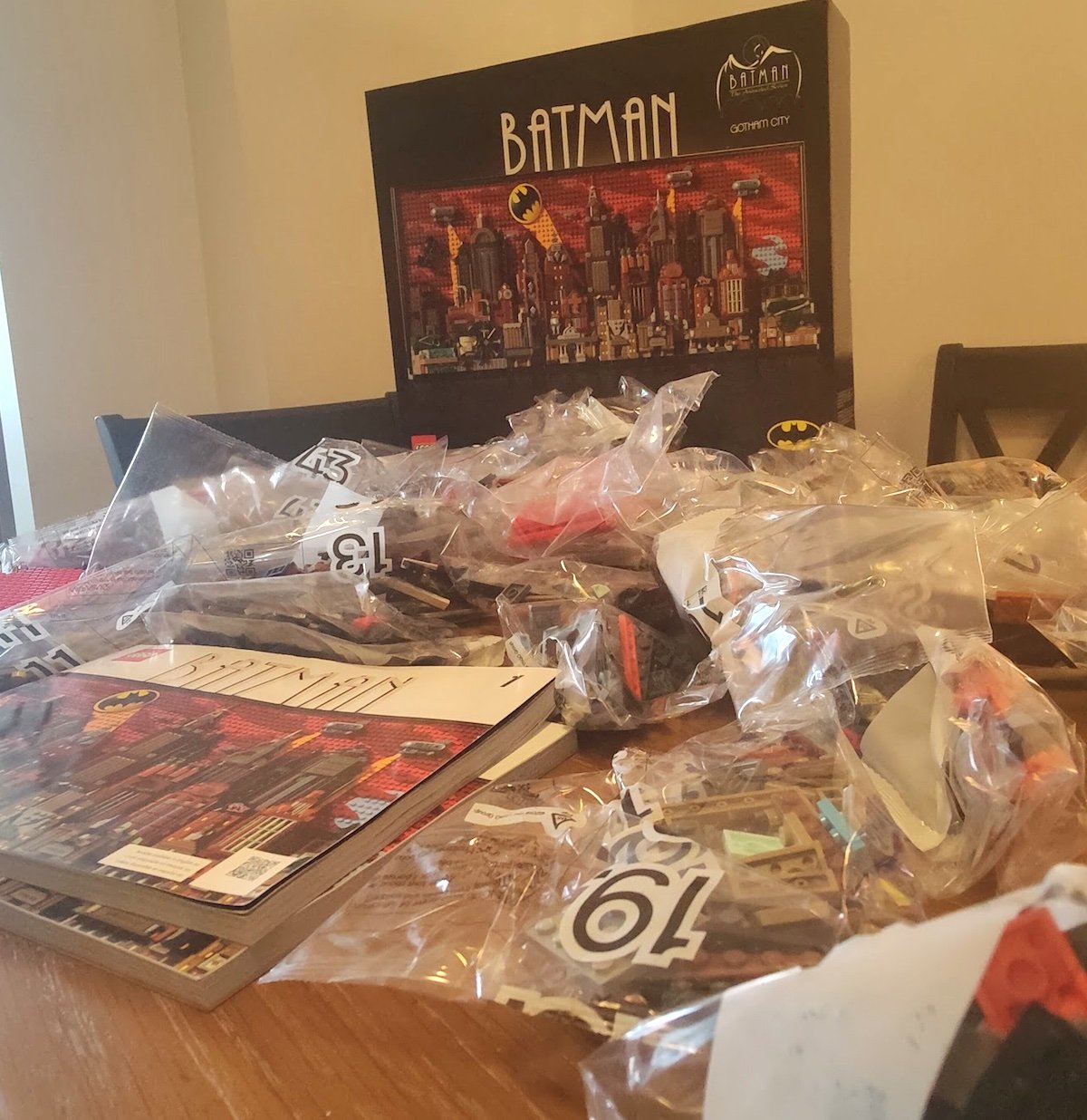 The LEGO Gotham City set with the box in the background with the bags of pieces and instruction booklets on a table in front