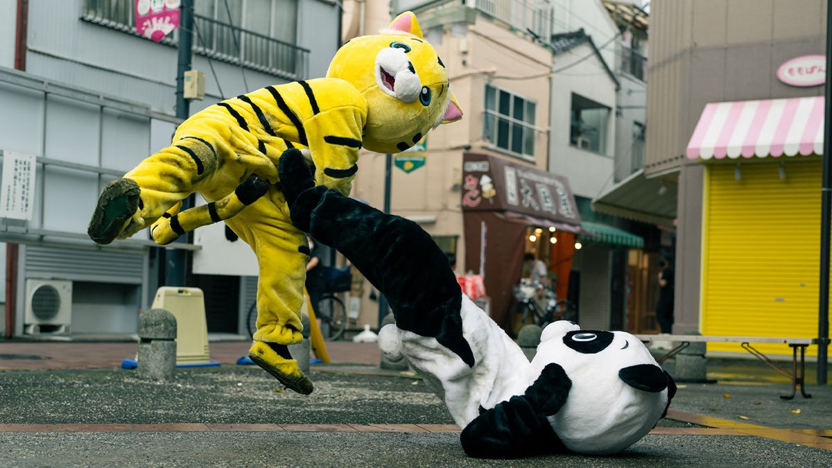 A fight between two people in large animal costumes, as a panda sitting on the ground kicks a leaping tiger in the stomach, in Baby Assassins 2