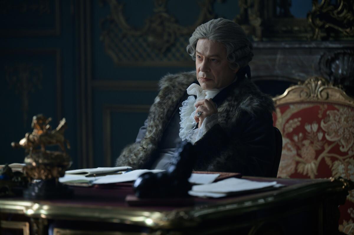 A man sits at a desk in a gilded chair.