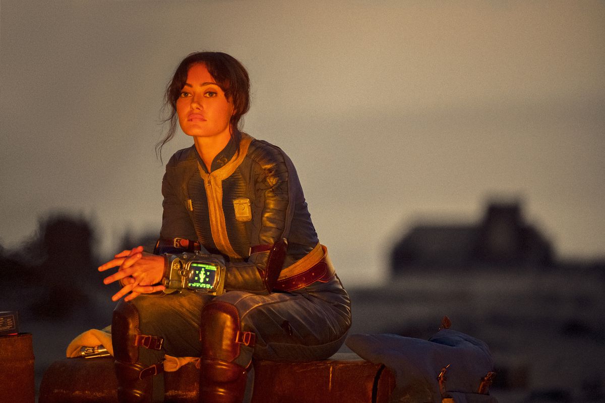 Lucy (Ella Purnell) sitting by a fire looking solemn in a still from Fallout