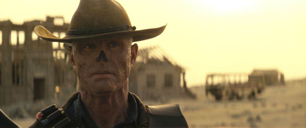 A close-up shot of the Ghoul, played by Walter Goggins standing in a barren field surrounded by derelict houses in the Fallout TV series.