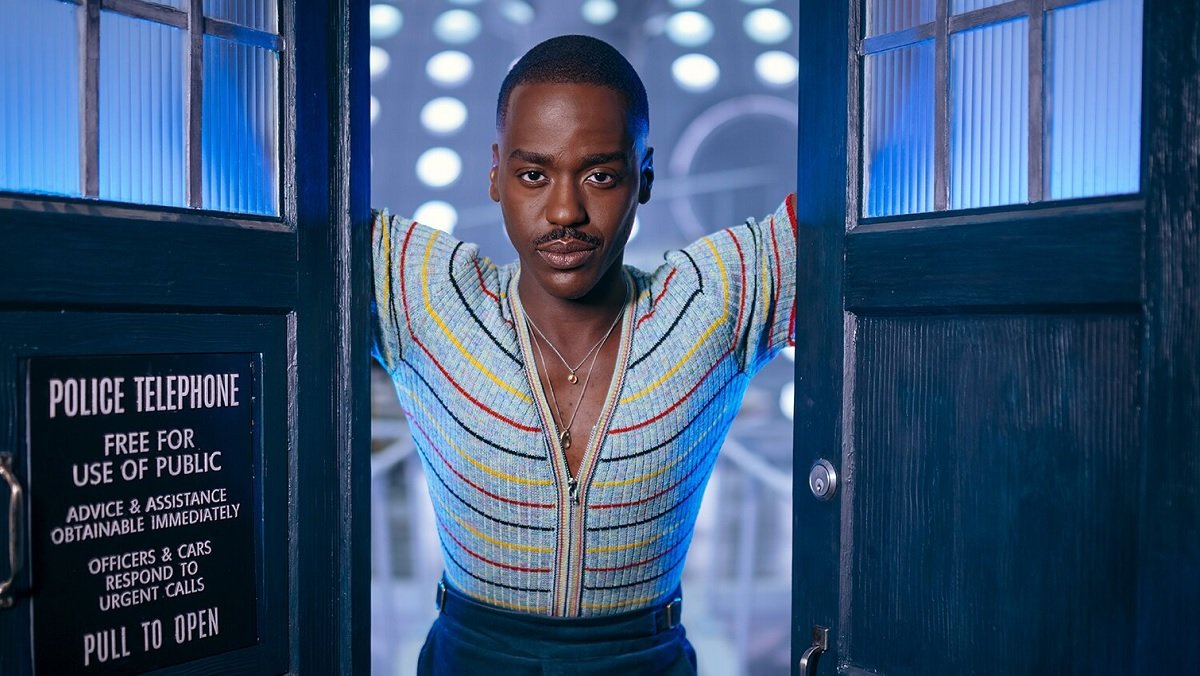 The Doctor (Ncuti Gatwa) stands between the open TARDIS doors and looks directly at camera.