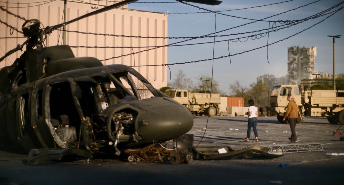 Two photojournalists walk past a crashed helicopter.
