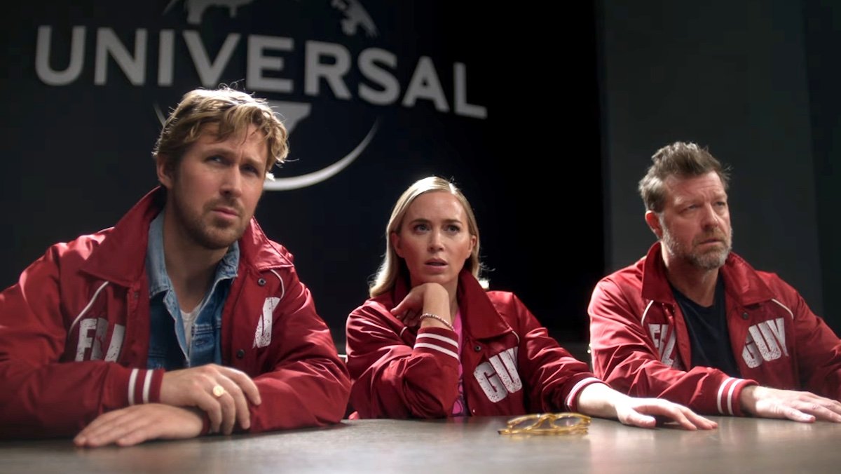 Ryan Gosling, Emily Blunt, and David Leitch in red coats at a table in The Fall Guy promos