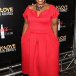 Mandisa smiling with her hands in the pocket of a tea-length short-sleeve red dress