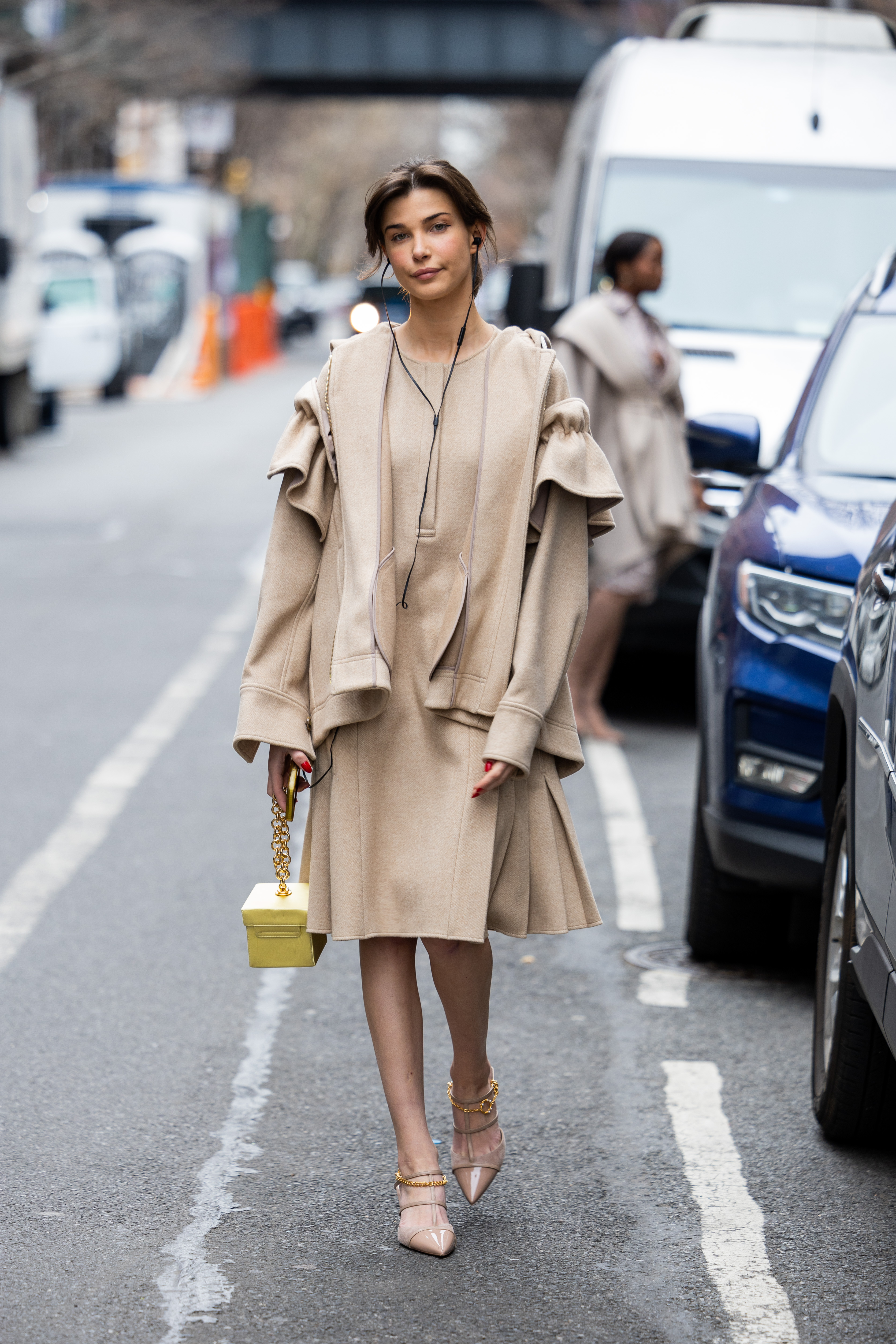 Charlotte Briar D'Alessio wears a beige dress, jacket, yellow bag, and pointed heels outside Adeam during New York Fashion Week on February 12, 2023, in New York City