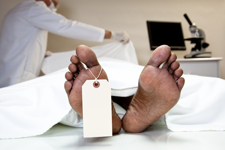 Mortician, coroner covering dead body in morgue. Feet, toe tag.