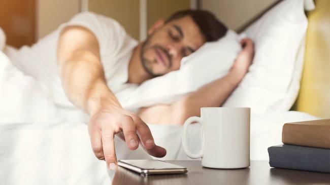 Man in bed reaching for iPhone