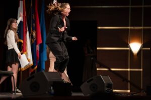 Cecilia Bartin, a participant in Missouri’s 2022 edition of the Girls State political event, jumps in the air while shouting on a stage while delivering a speech in the documentary Girls State