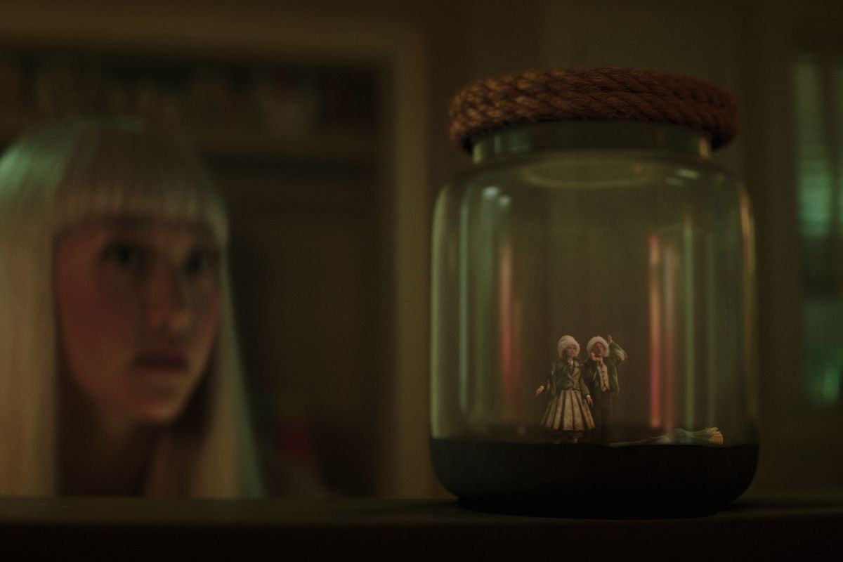 A girl looking at a jar containing two tiny sprites