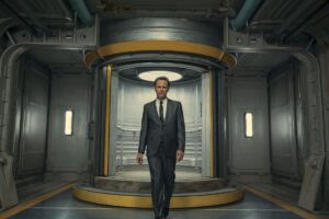 A still of Walton Goggins walking out of a Vault door in a suit, talking to the camera