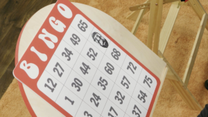A giant bingo board, on which one number, 71, has been marked with a large ink stamp in the shape of Sam Reich’s head, in Game Changer’s “Bingo.”