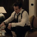 Colin Farrell pours a glass of scotch in suspenders with his tie loosened in the Apple TV Plus show Sugar
