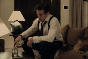 Colin Farrell pours a glass of scotch in suspenders with his tie loosened in the Apple TV Plus show Sugar