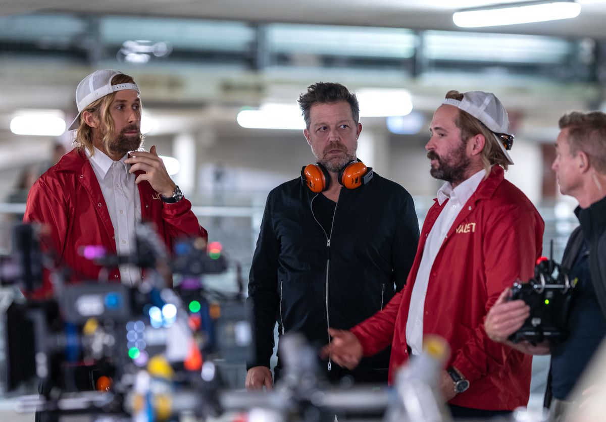 Ryan Gosling and stunt performer Logan Holladay, both wearing red valet jackets, talk to David Leitch on the set of The Fall Guy