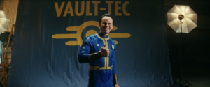 Cooper Howard (Walton Goggins) holding a thumbs up in a Vault-Tec suit during a photo shoot in a still from Fallout episode 3
