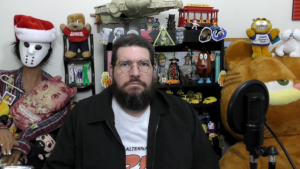 Russ Hoover sitting in a room full of nerd memorabilia, including a Garfield. He has a very serious expression.