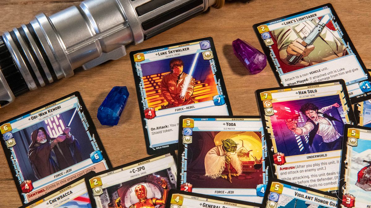 An assortment of cards from the Luke Skywalker starter deck near several kyber crystals and a lightsaber.