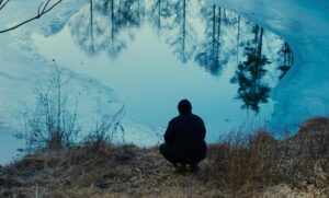 A man sits by a pond.