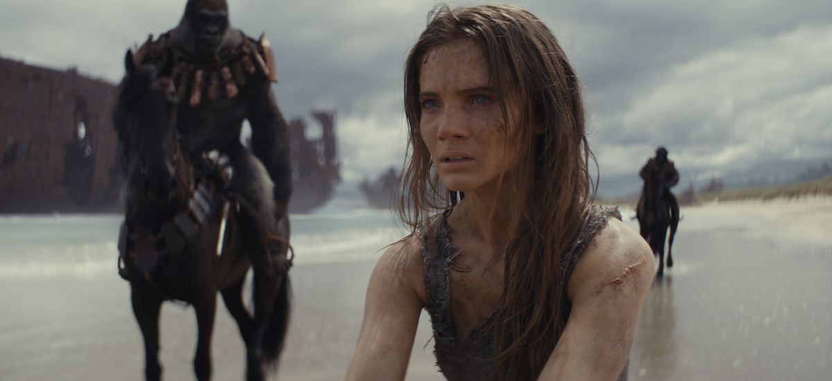 The human Mae (Freya Allen) sits on a beach with apes on horseback behind her in Kingdom of the Planet of the Apes