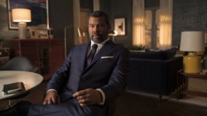 Jordan Peele sitting in a suit as the Twilight Zone host
