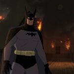 Batman, looking very 1940s serial inspired, stands in front of a burning building in Batman: Caped Crusader.