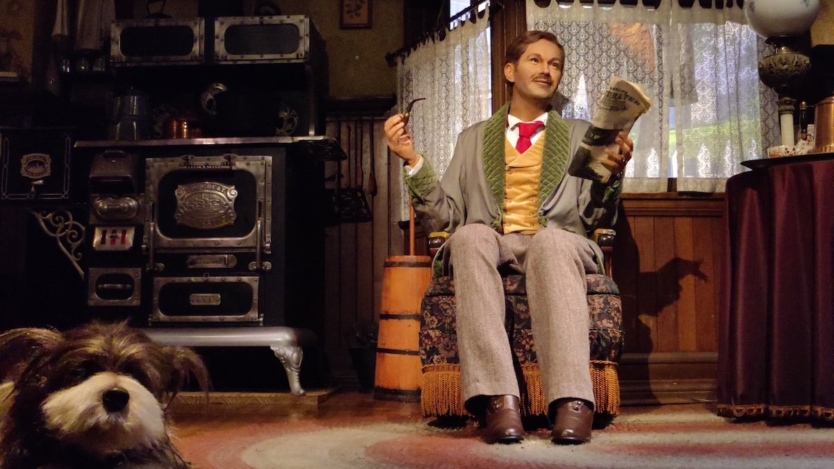 An animatronic man with a mustache sits in a chair in his old timey house with a dog on the floor on the Carousel of Progress at Magic Kingdom