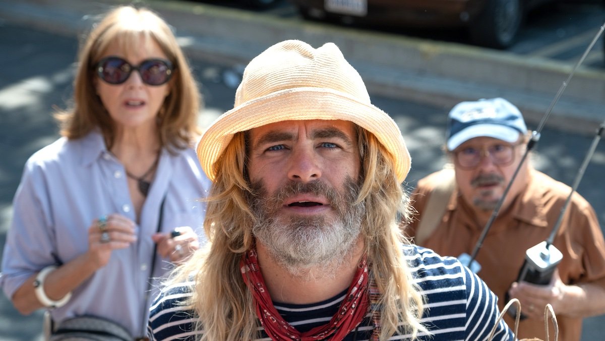 A long-haired, bearded Chris Pine with a hat in front of Annette Benning and Danny DeVito in Poolman