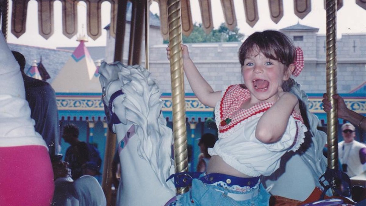 A young toothlee girl smiles sitting atop a horse on a carousel