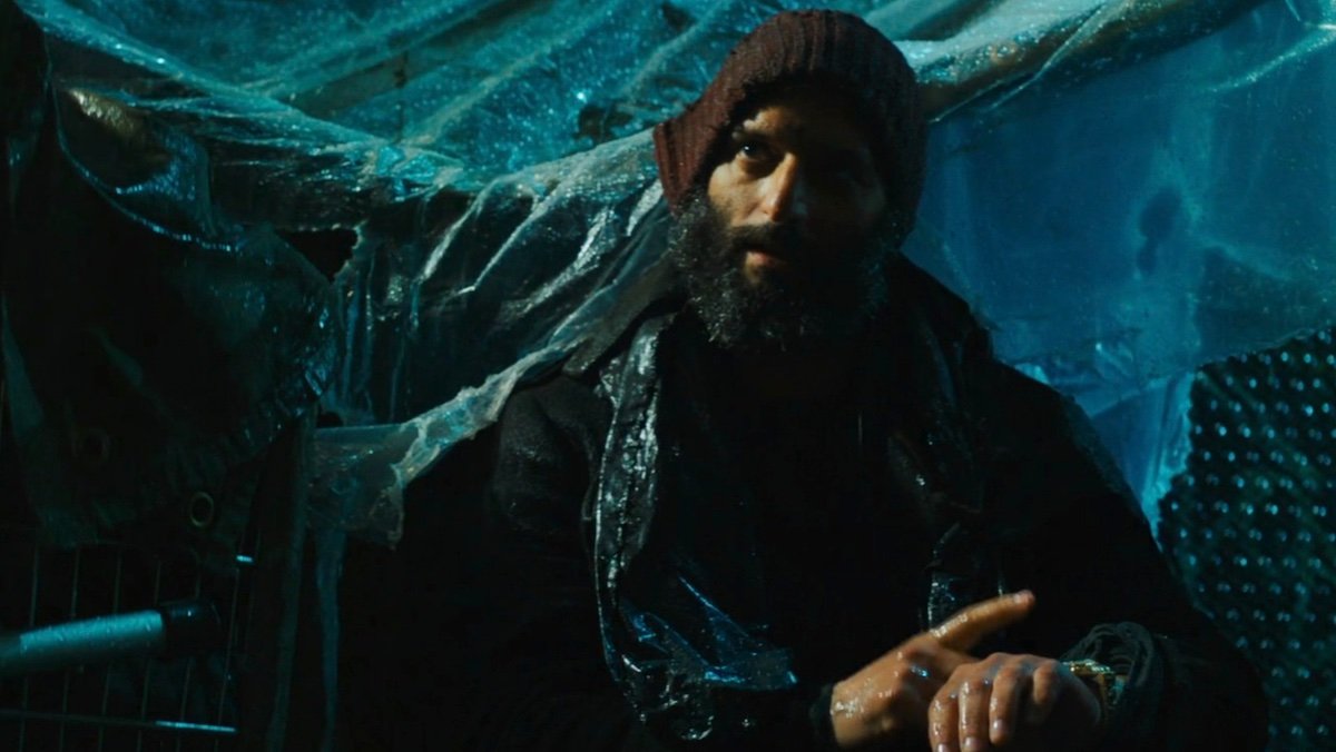 Jason Mantzoukas dressed an unhoused man sitting in the rain tapping his watch in John Wick: chapter 3
