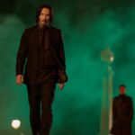 Keanu Reeves walks away from two men and a smoky green sky in John Wick: Chapter 4