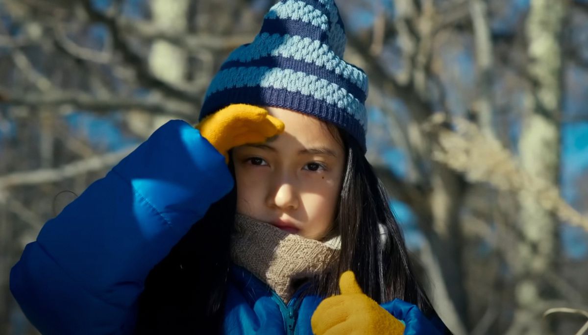 Hana (Ryo Nishikawa), a young Japanese girl in a puffy coat and knit hat, shades her eyes with her hand and looks doubtfully into the camera in Ryûsuke Hamaguchi’s Evil Does Not Exist
