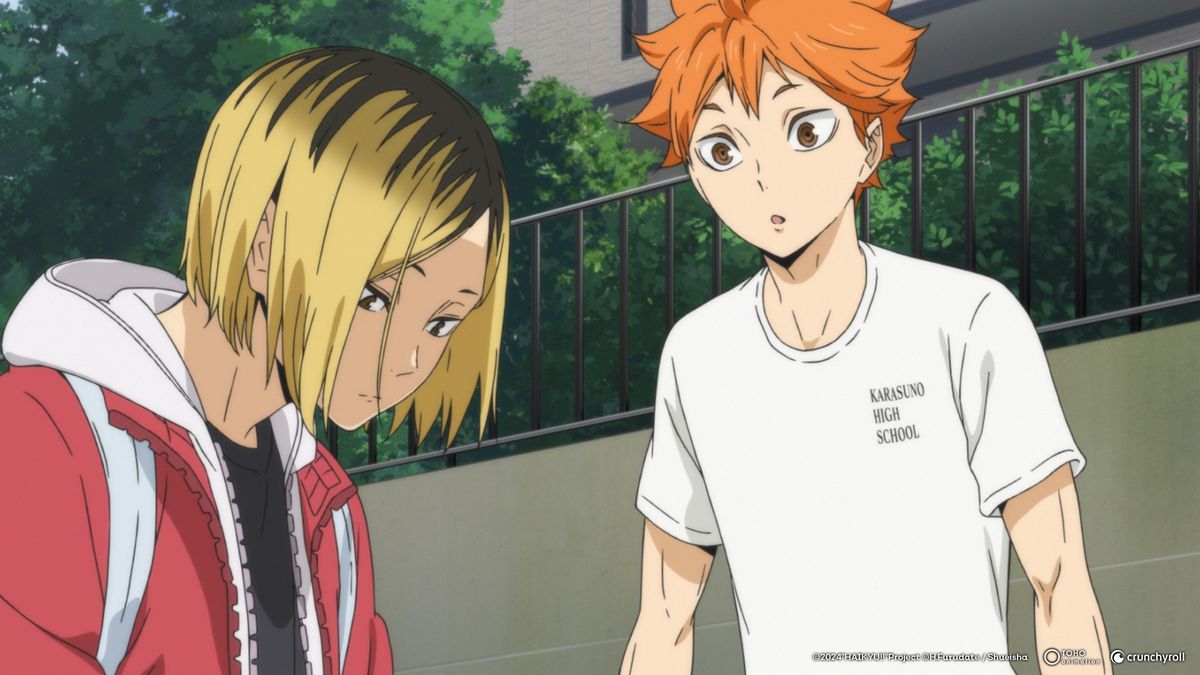 A blonde boy in a red track suit sits down, while an orange haired boy in a white t-shirt looks curiously at him