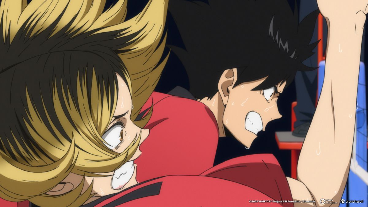 A blonde boy and a dark-haired boy growl as they intensely play volleyball. Both wear red shirts.
