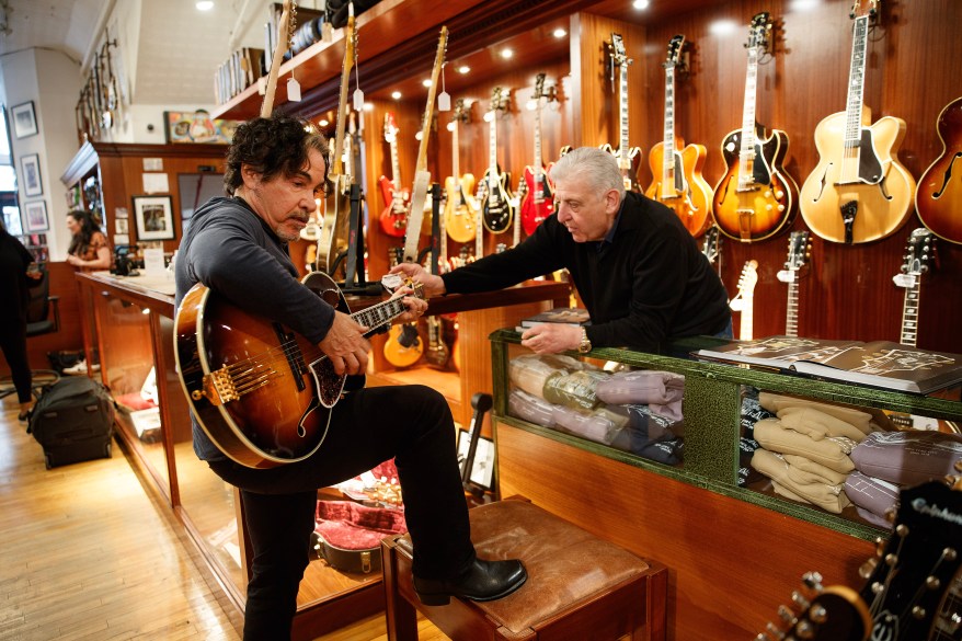 Rudy's Music owner Rudy helping Oates with an acoustic guitar.