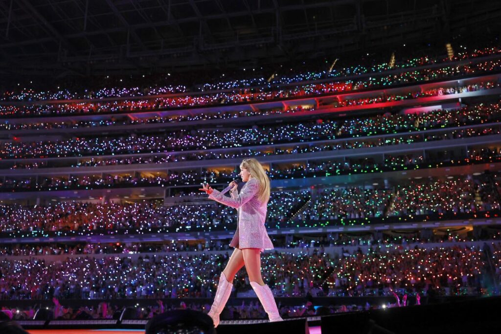 Taylor Swift performs onstage in front of a sea of thousands of people at a stadium