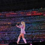 Taylor Swift performs onstage in front of a sea of thousands of people at a stadium