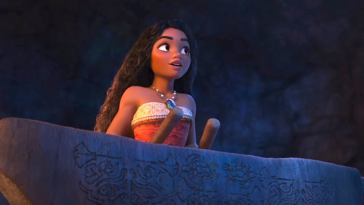 Moana holds two clubs over a stone altar in a dark cave with carvings in Moana 2