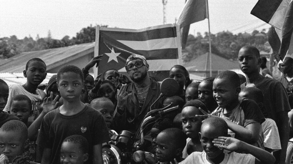 Rafa Pabön posing with kids from an African village in front of a Puerto Rican flag.