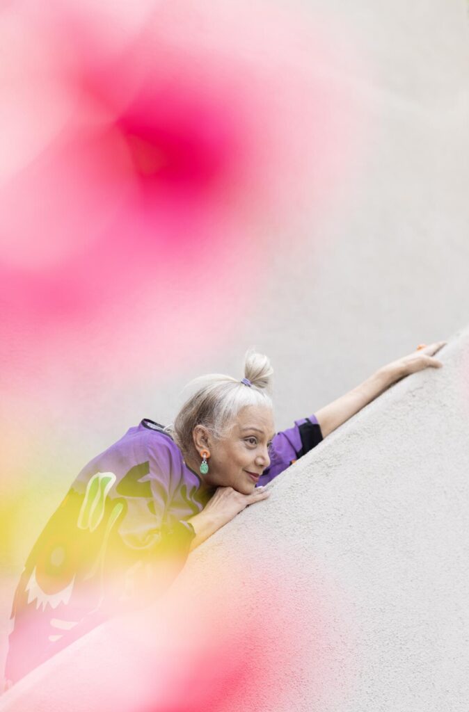 A woman leans on a stairway surrounded by flowers.