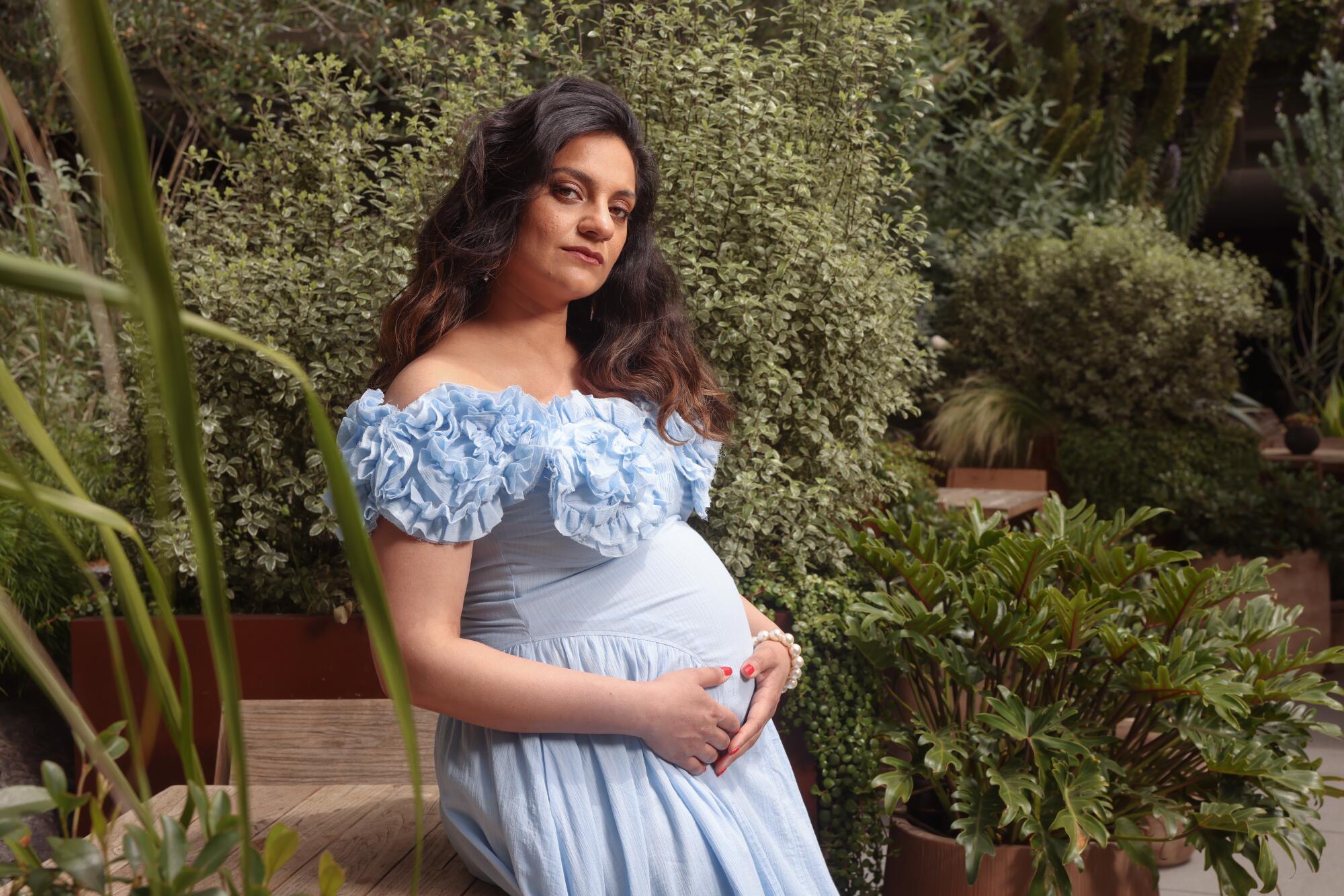 Nida Manzoor leaning near some greenery.