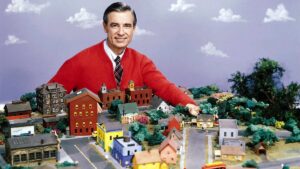 Mister Rogers in his cardigan sweater, standing before the set of the Neighborhood of Make Believe.