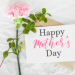 craft envelope, white sheet of paper, one pink carnation and green leaves, inscription text happy mother's day, holiday and sweet wishes concept