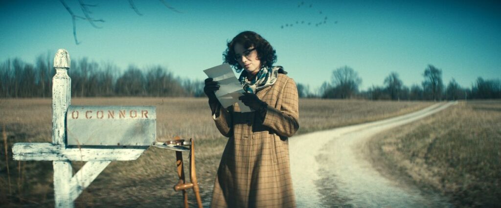 Maya Hawke as Flannery O’Connor, opening a letter from her mailbox and looking at it quizzically