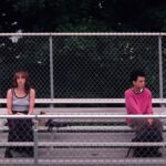 Super-awkward teenage sorta-friends Maddy (Brigette Lundy-Paine) and Owen (Justice Smith) sit far apart from each other on their school’s outdoor metal bleachers in I Saw the TV Glow