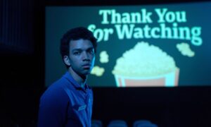 Twentysomething movie-theater employee Owen (Justice Smith) stands in a dark theater and looks at the camera, with a slide on the screen behind him that says “Thank You for Watching” atop a cartoon bucket of popcorn in Jane Schoenbrun’s I Saw the TV Glow